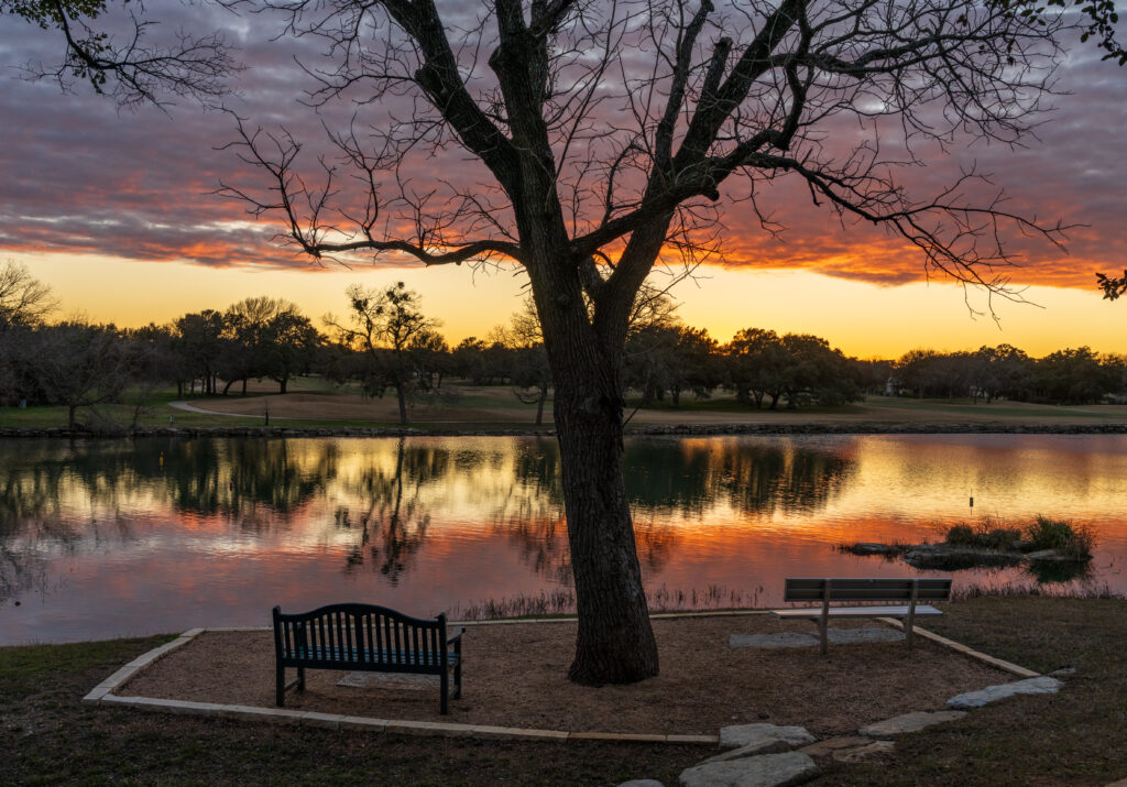 Dramatic sunset lighting a layer of clouds and reflected in the still water of Legacy Hills Park near Georgetown, Texas with seats
