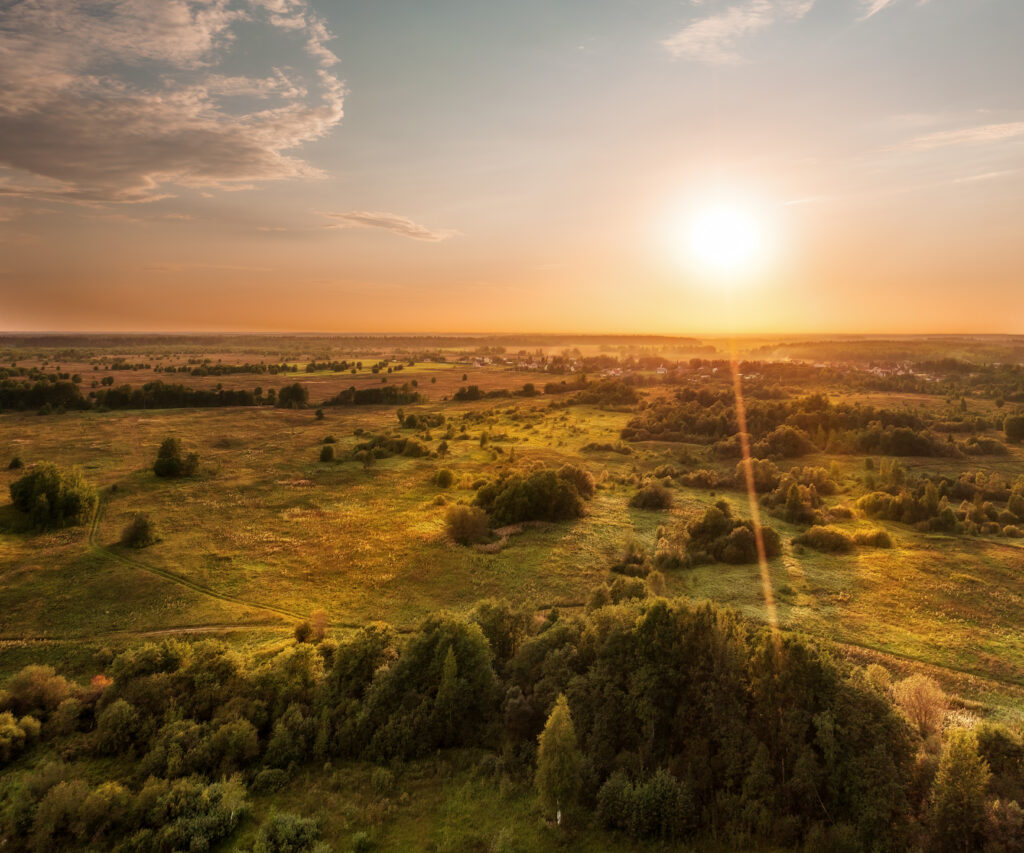 Aerial scenic landscape of forested plain at sunset. Bright colored sky and green plain, sun visible