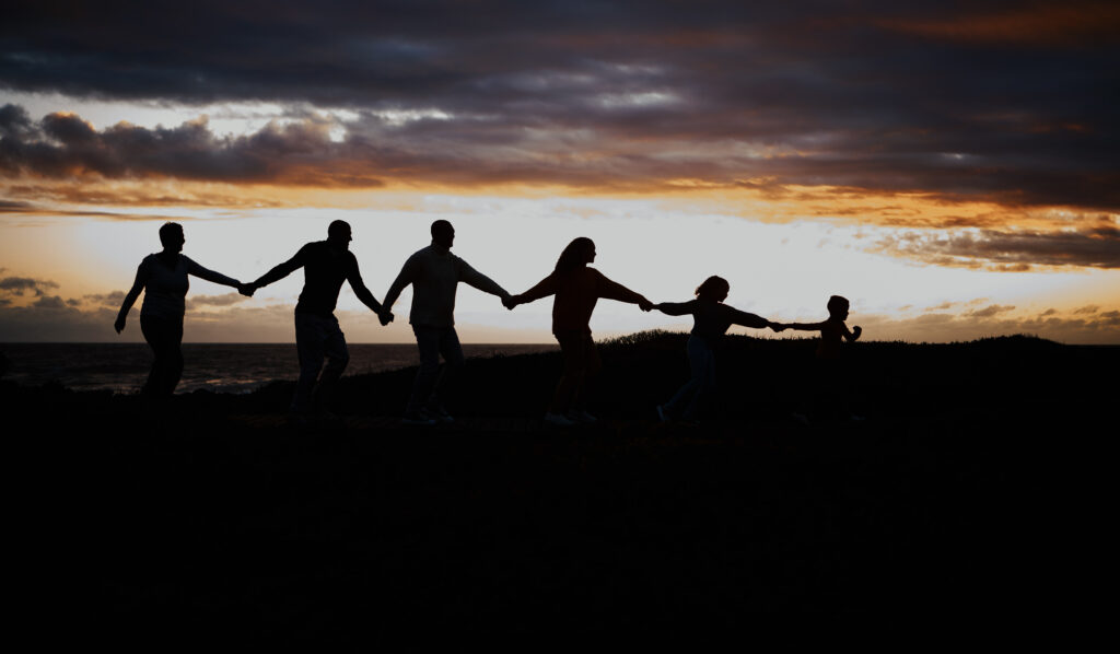 Sunset, beach and silhouette of family with children by ocean for bonding, quality time and peace. Shadow, nature and grandparents, parents and kids holding hands on vacation, holiday and weekend