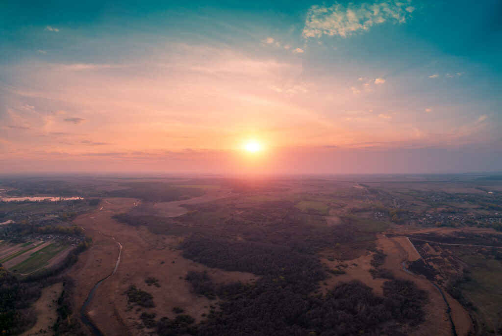 Spring rural landscape in the evening with beautiful burning sky. Aerial view. Panoramic view of pine forest, fields, river, and village during blazing sunset