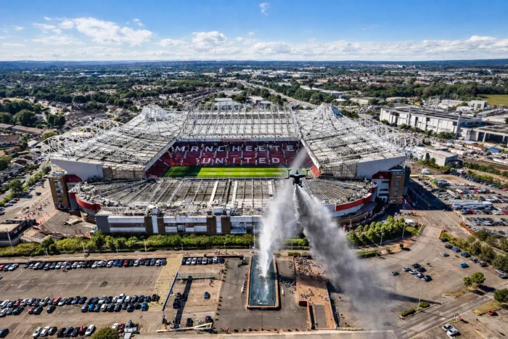 Aerial view of Old Trafford stadium with a drone scattering ashes above a fountain.