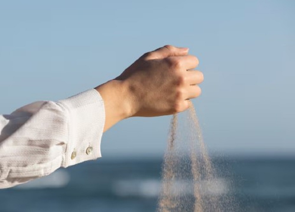 Hand scattering ashes against a blurred ocean background under a clear sky.
